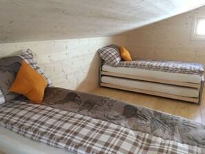 Avokeittiötyylinen huone, jossa on korkea katto ja näkyvillä olevat puupalkit. Huoneessa on kaksi sänkyä, joissa on ruutukuviolliset vuodevaatteet ja kuviollinen päiväpeitto.