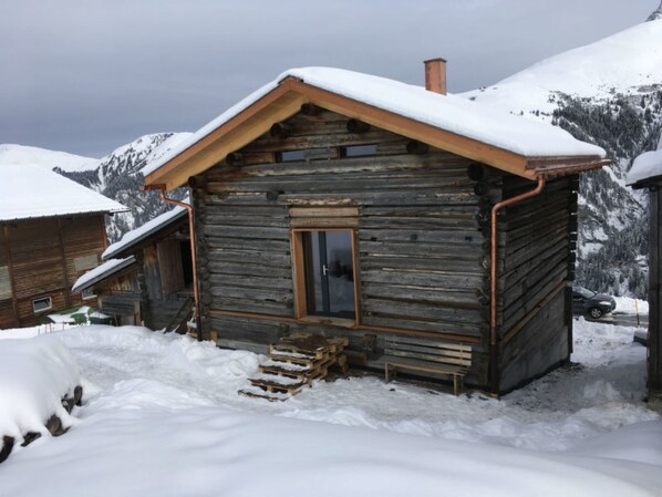 Une cabane rustique en rondins de bois, avec une porte en bois, une cheminée et un toit recouvert de neige.