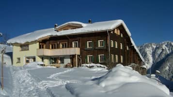 Un chalet a più piani con tetto innevato e una pista da sci in primo piano.