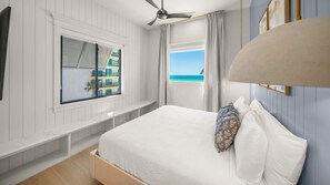 A bedroom with a bed, a ceiling fan, a window with a view of buildings, and a view of the ocean. - Pool, Spa & Rooftop Retreat - Direct Beach Access (Clearwater)