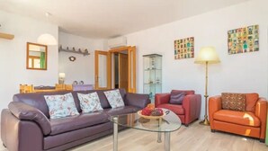 Ein Wohnzimmer mit einem violetten Sofa, einem Glastisch, einem roten Sessel und einem orangenen Sessel sowie einer Stehlampe.