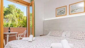 Ein Schlafzimmer mit einem Bett, einem kleinen Tisch mit Stühlen und einem Fenster mit Blick auf Bäume.