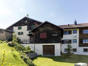 Un edificio de dos plantas con un amplio portón de garaje, un balcón y un muro de piedra.