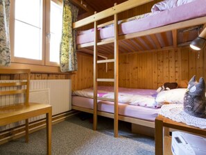Ein Schlafsaal mit Etagenbetten, Holzboden, Schreibtisch, Stuhl und Heizkörper.