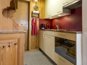 Eine kompakte Küche mit Holzschränken, einer roten Spritzschutzwand und einem eingebauten Backofen.