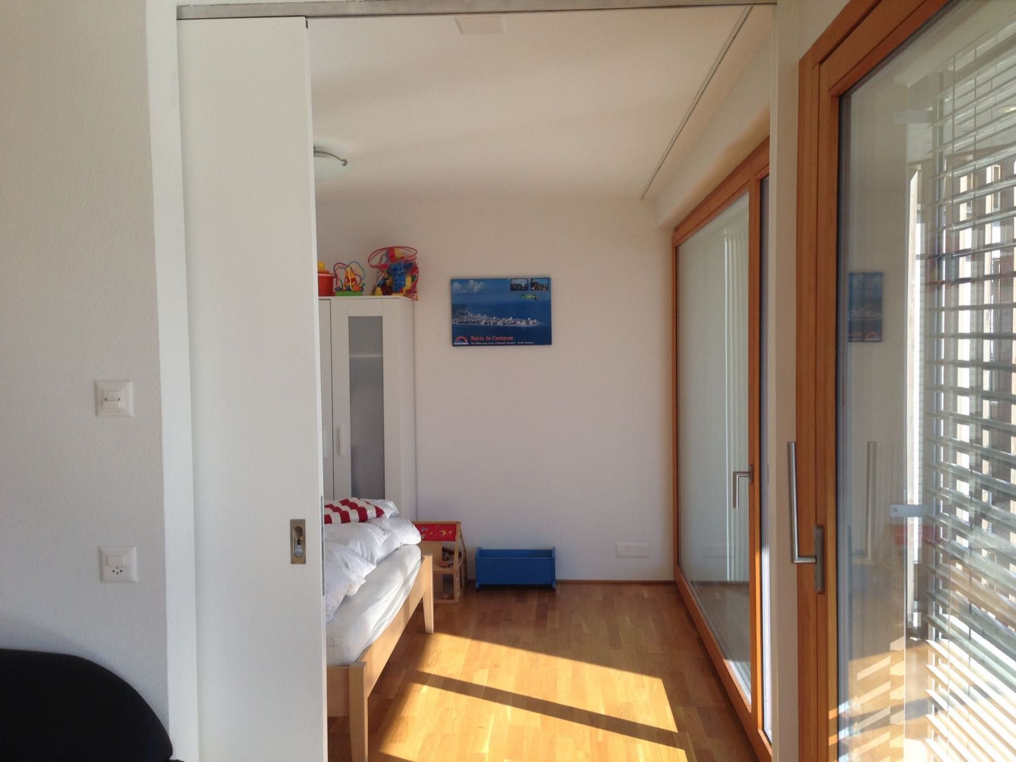Ein Schlafzimmer mit einem Bett, einem kleinen Tisch, einer blauen Aufbewahrungsbox und einem Poster an der Wand.