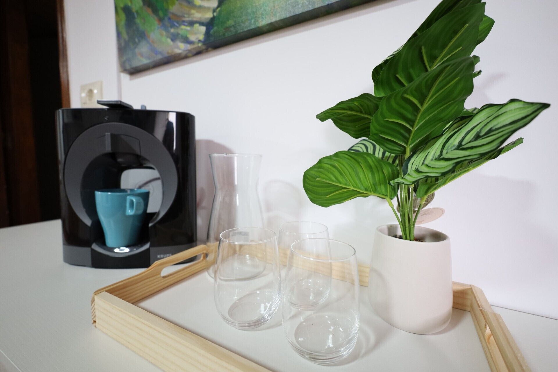 Une machine à café, une tasse bleue, une plante en pot et quatre verres sur un plateau.