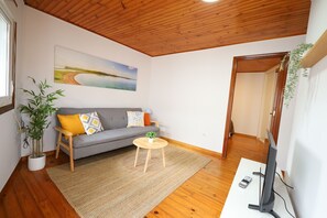 Un salon avec un canapé gris, une table basse en bois, un tél éviseur et un tableau accroché au mur.