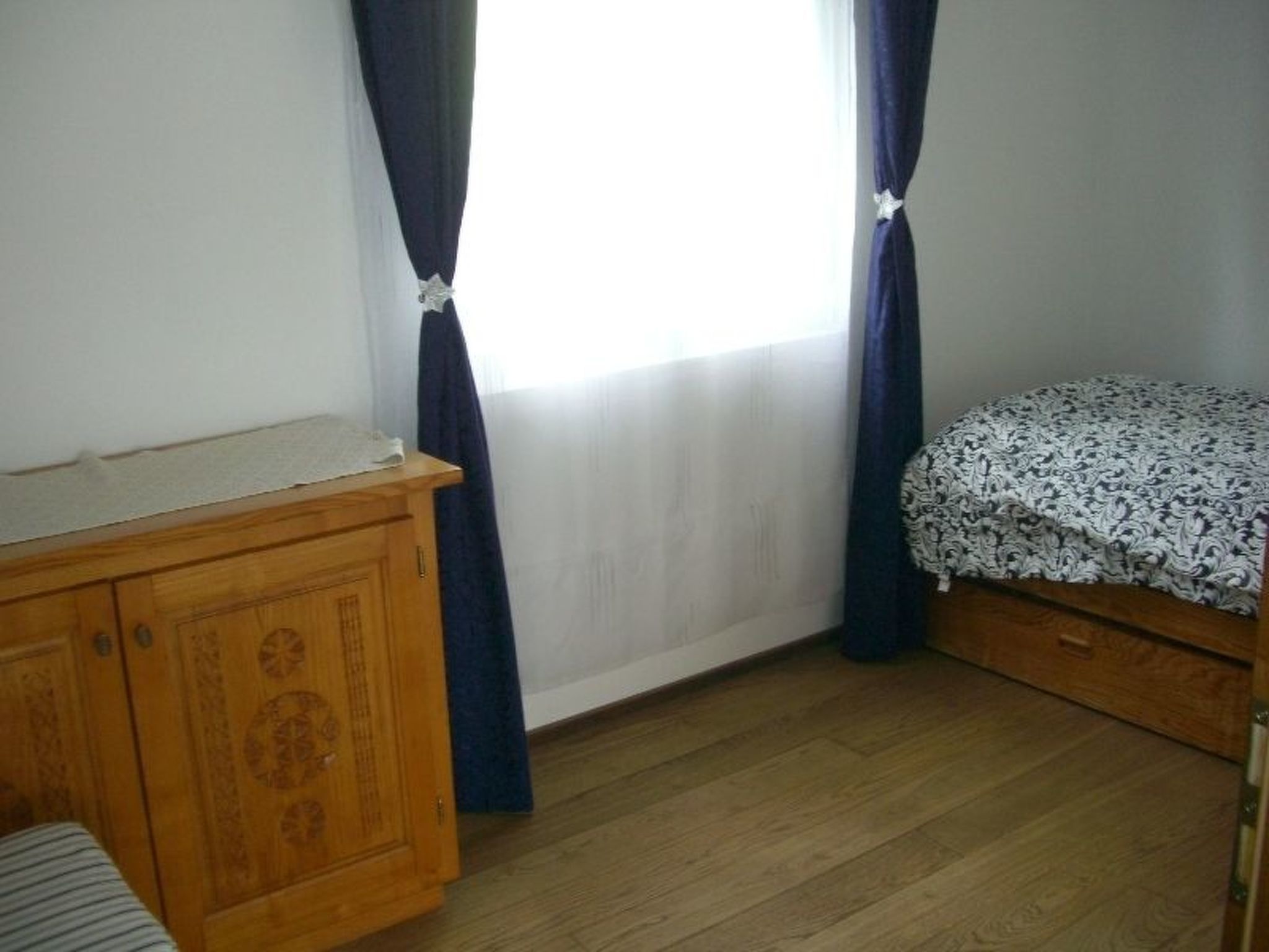 Een slaapkamer met een houten garderobe, een bed met beddengoed met een patroon en een raam met gordijnen.