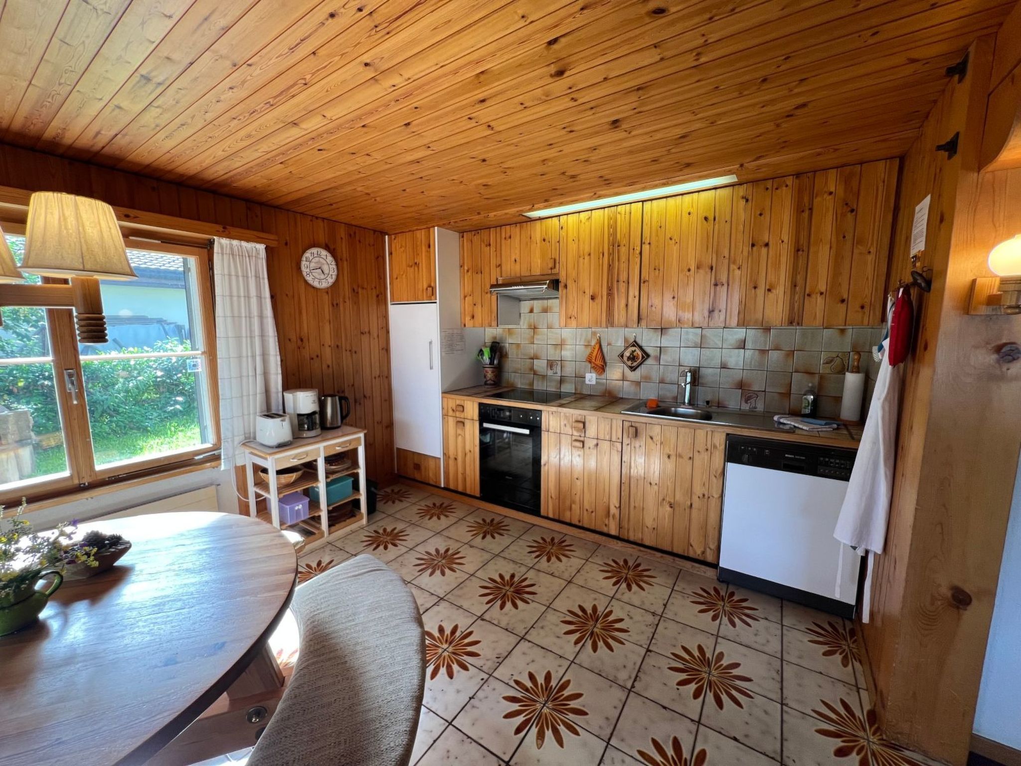 Eine Küche mit Holzwänden, einem Essbereich, einer Uhr und Blick durch ein Fenster.