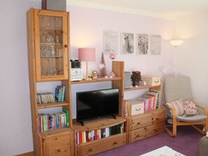 A living room with a television, wooden bookshelves, a chair, and decorative items.