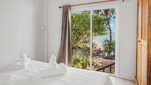 A hotel room with a bed, white towels, a view of a beach, and a sliding glass door. - Room-charming Guest Room Retreat in Mare (Koh Samui)