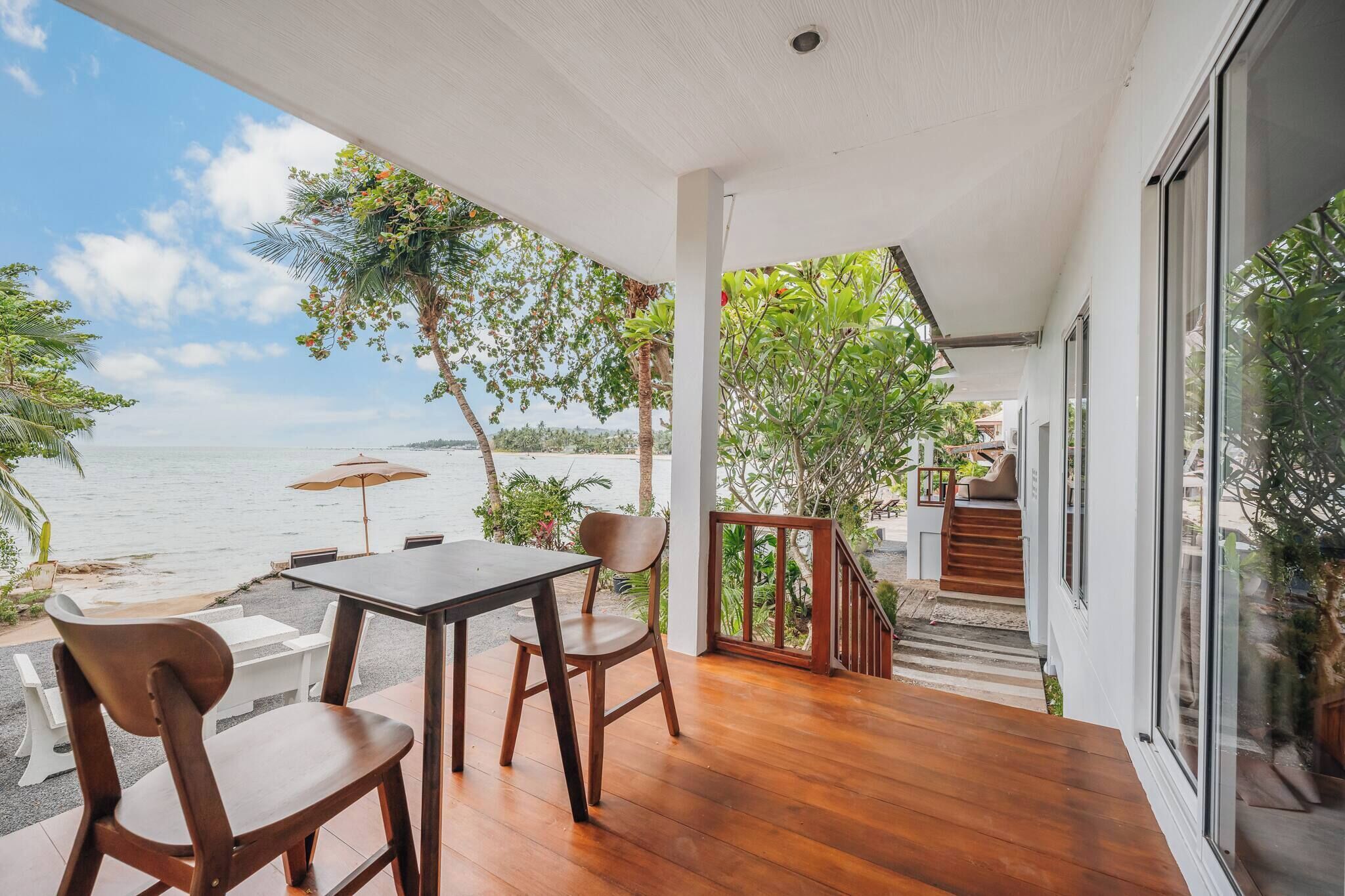 A wooden deck with a table and chairs, overlooking a beach and ocean.