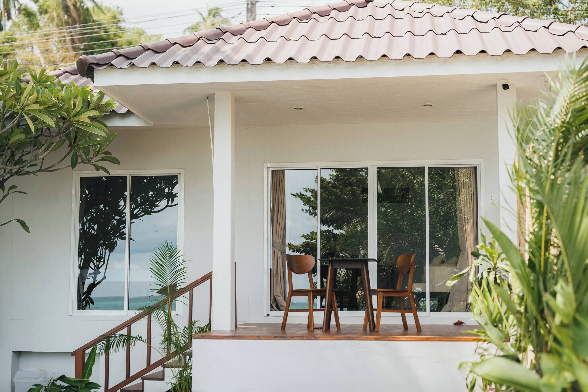 A modern house with a tiled roof, a balcony with a table and chairs, and large windows offering a view of the outdoors.