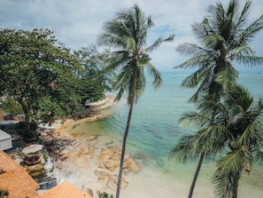 Uma praia com águas turquesa cristalinas, palmeiras e um litoral rochoso.
