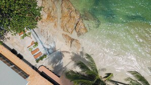 An aerial view of a beach with clear water, rocky shoreline, and palm trees. - Room-charming Guest Room Retreat in Mare (Koh Samui)