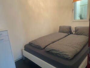 Quarto pequeno com uma cama de solteiro, armário branco e espelho sobre a cama.