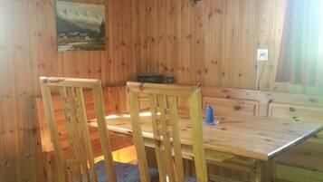 Ein Esszimmer mit Holzboden, einem Tisch, Stühlen, einer Hängelampe und einem Bild an der Wand.