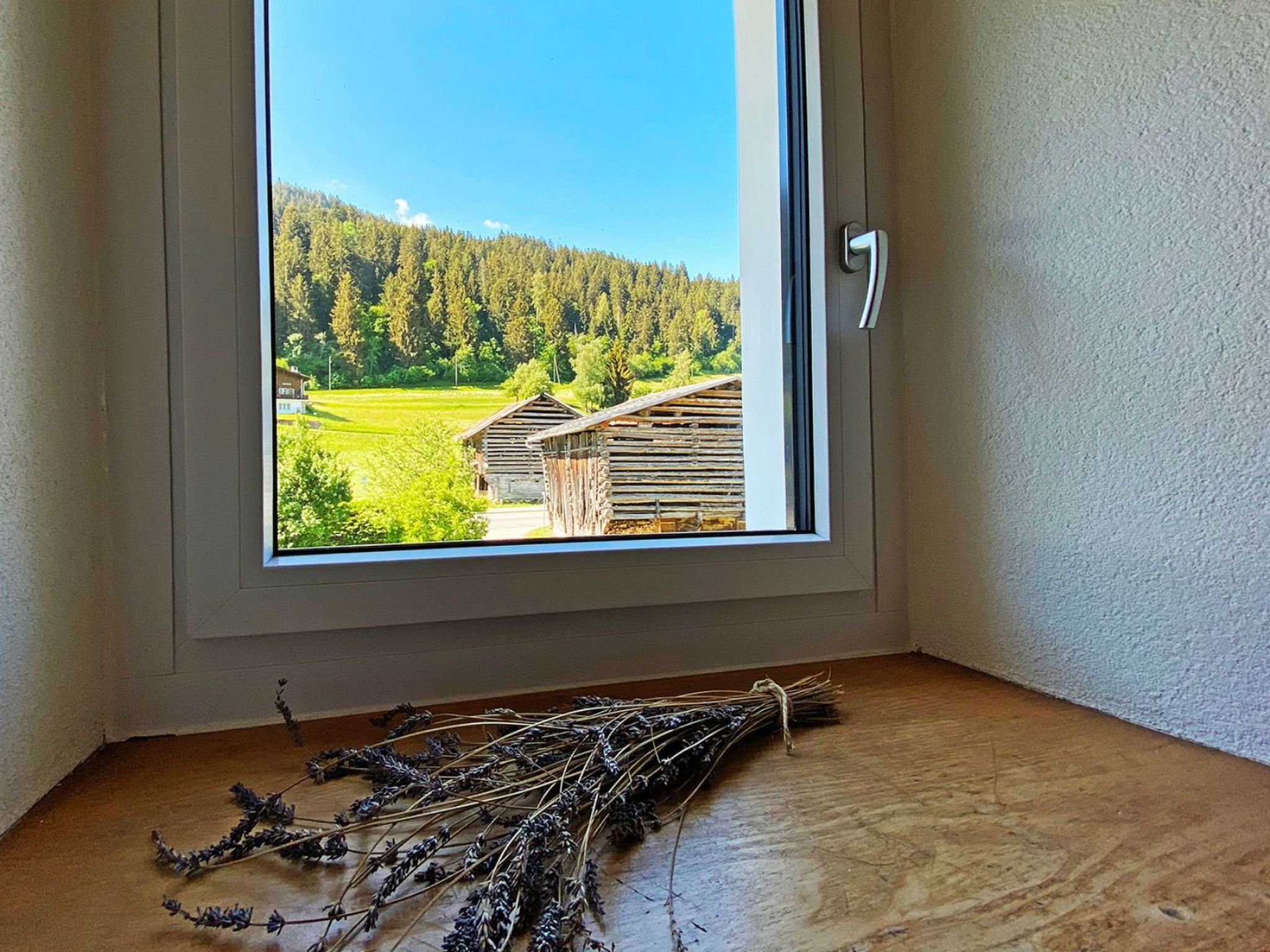 A room with a window overlooking a forested area and a wooden structure.
