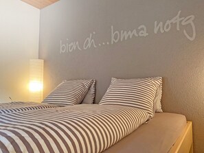 Ein Schlafzimmer mit einem Bett, zwei Kissen, einer Wand mit Schrift und einer Nachttischlampe.