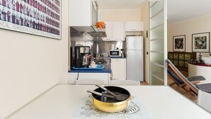 Une cuisine compacte équipée d’un four à micro-ondes, d’une cuisinière et d’un réfrigérateur. Une table à manger avec un set de table est placée au premier plan.