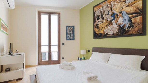 Une chambre d’hôtel avec un lit, un bureau, une chaise, un tableau et une porte.