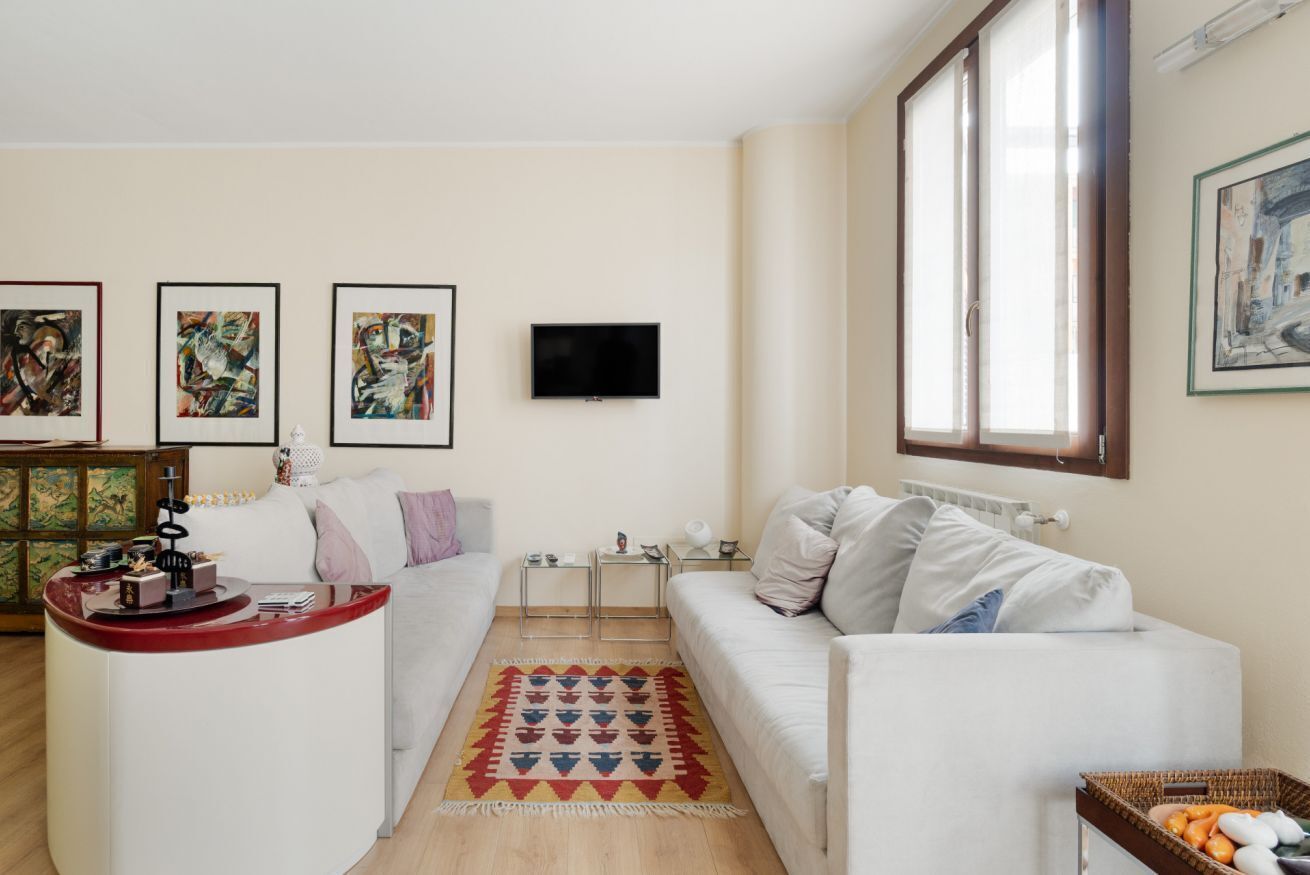 Een woonkamer met een witte bank, een salontafel, een televisie en kunst aan de muur.