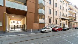 Un immeuble doté d’une entrée moderne, avec des voitures garées devant et une rue dégagée.