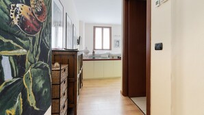 Un couloir menant à une cuisine dotée d’un plancher en bois, d’une fenêtre et d’une porte.