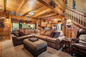 A cozy cabin interior with a wooden ceiling, a large L-shaped leather sofa, a dining table, and a kitchen area. - Swan Way Mountain Retreat (Lake Lure)