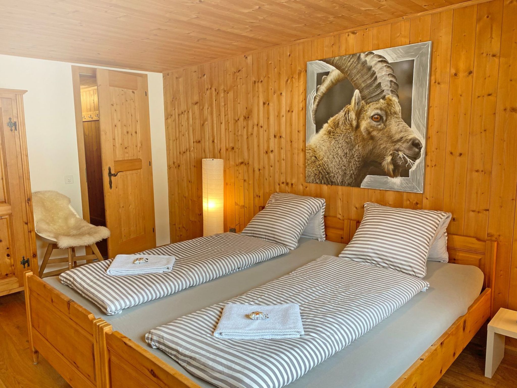 A wooden cabin room with two single beds, a chair, and a large framed picture on the wall.