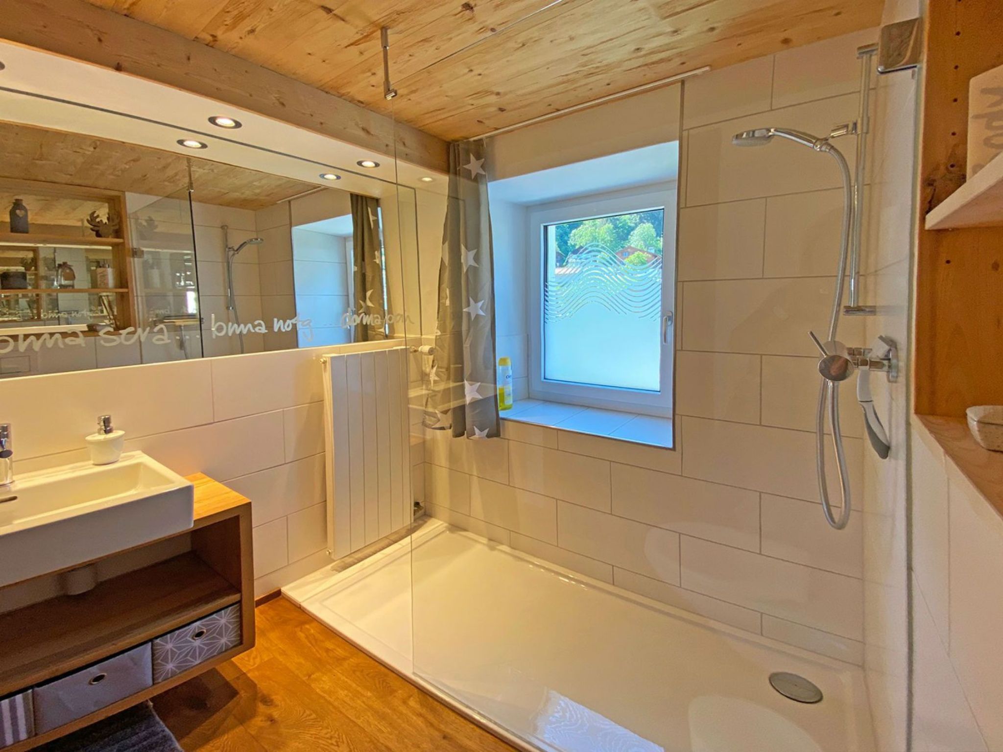 Un baño moderno con ducha envuelta en vidrio, un espejo grande y una ventana.