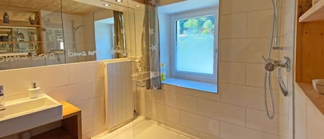 Un baño moderno con ducha envuelta en vidrio, un espejo grande y una ventana.