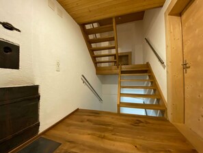 Una escalera de madera que conduce a un piso superior, con una puerta a la derecha y un interruptor de luz en la pared a la izquierda.