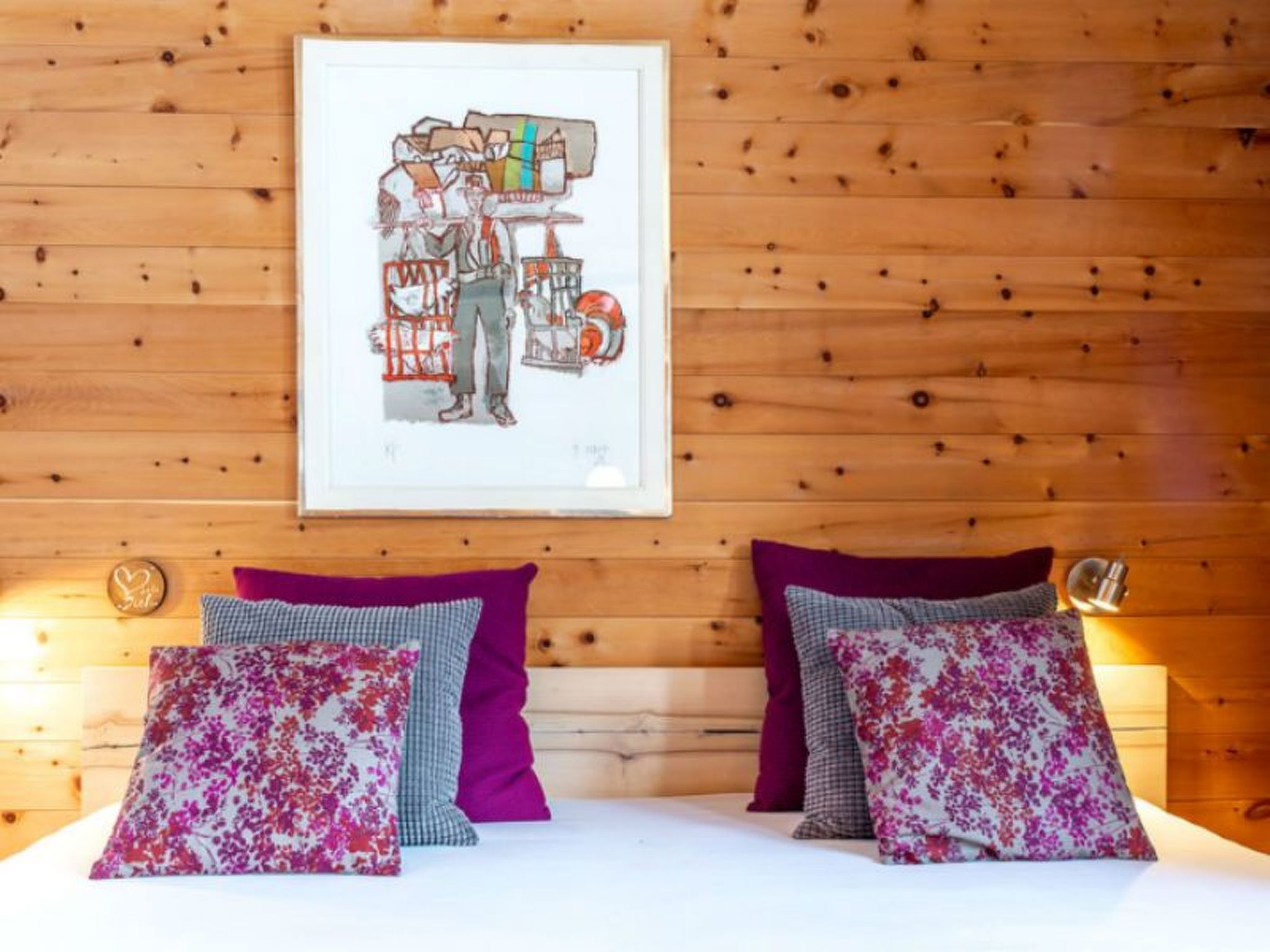 A room with wooden walls, a framed artwork, and two beds with floral-patterned pillows.