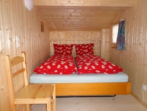 A small wooden room with a bed, a chair, and a window with curtains.