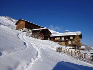 A snow-covered slope with a wooden building and a smaller structure on the right.