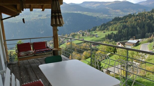 Ein Balkon mit Tisch und Stühlen, mit Blick auf eine gebirgige Landschaft.