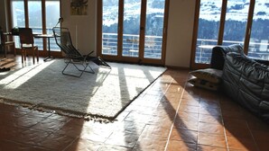 Ein geräumiges Wohnzimmer mit großem Fenster, einer Couch, einem Sessel und einem Teppich.