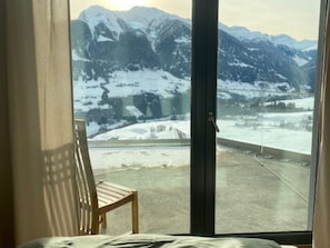 A room with a large window offering a view of snow-covered mountains and a road. - Schwalbennest Votteler, Morissen, (Morissen), 43009B by Interhome (Morissen)