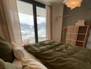 A room with a bed, a wooden wardrobe, and a view of mountains through a large window. - Schwalbennest Votteler, Morissen, (Morissen), 43009B by Interhome (Morissen)