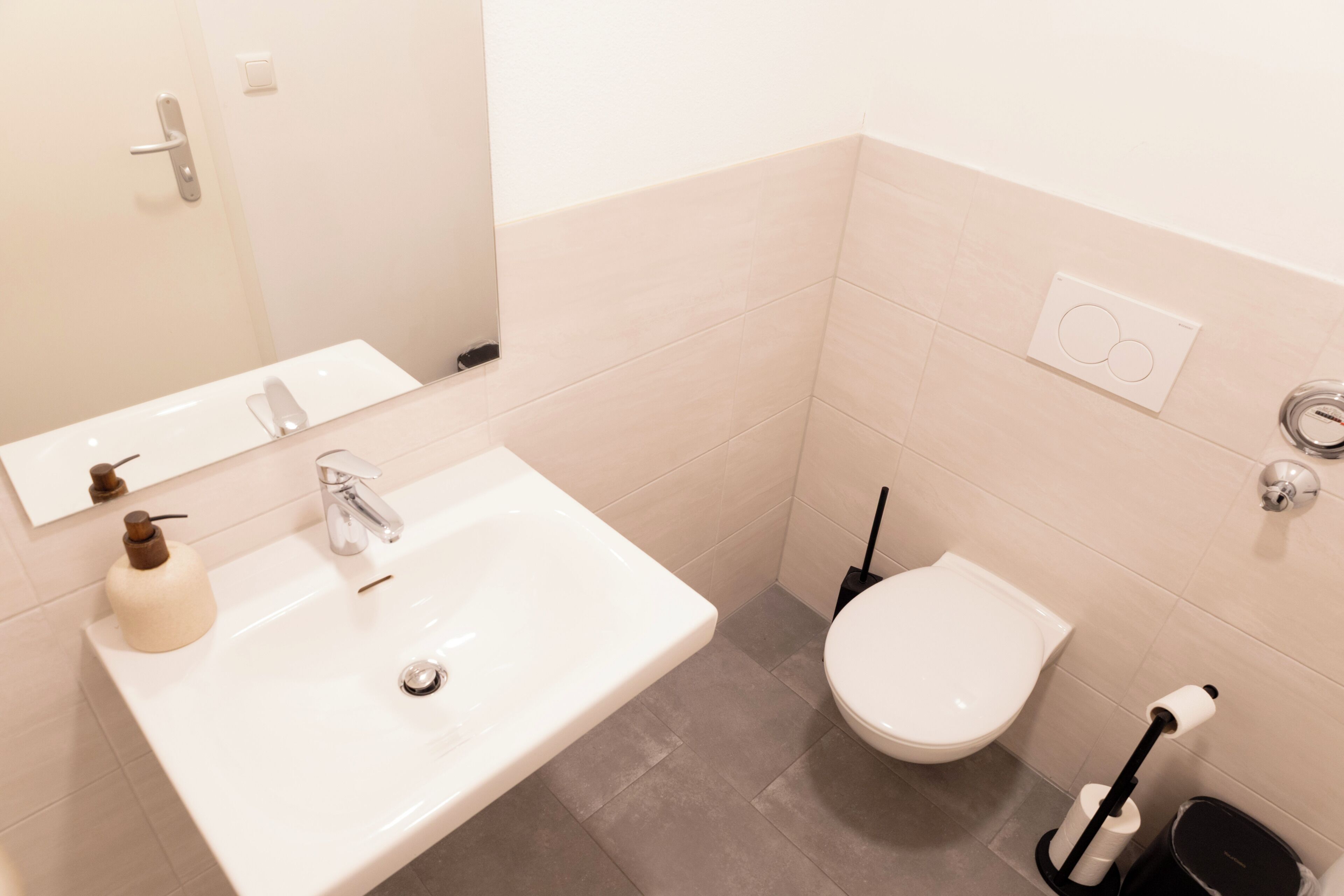 A bathroom with a white sink, a toilet, a mirror, and a hand dryer.