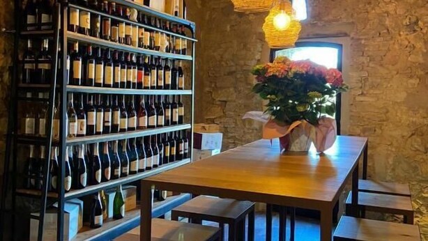 A rustic wine cellar with wooden shelves, hanging lights, and a stone wall.