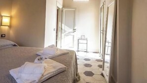 A hotel room with two beds, a wooden ceiling, a hallway with hexagonal tiles, and a door leading to a balcony.