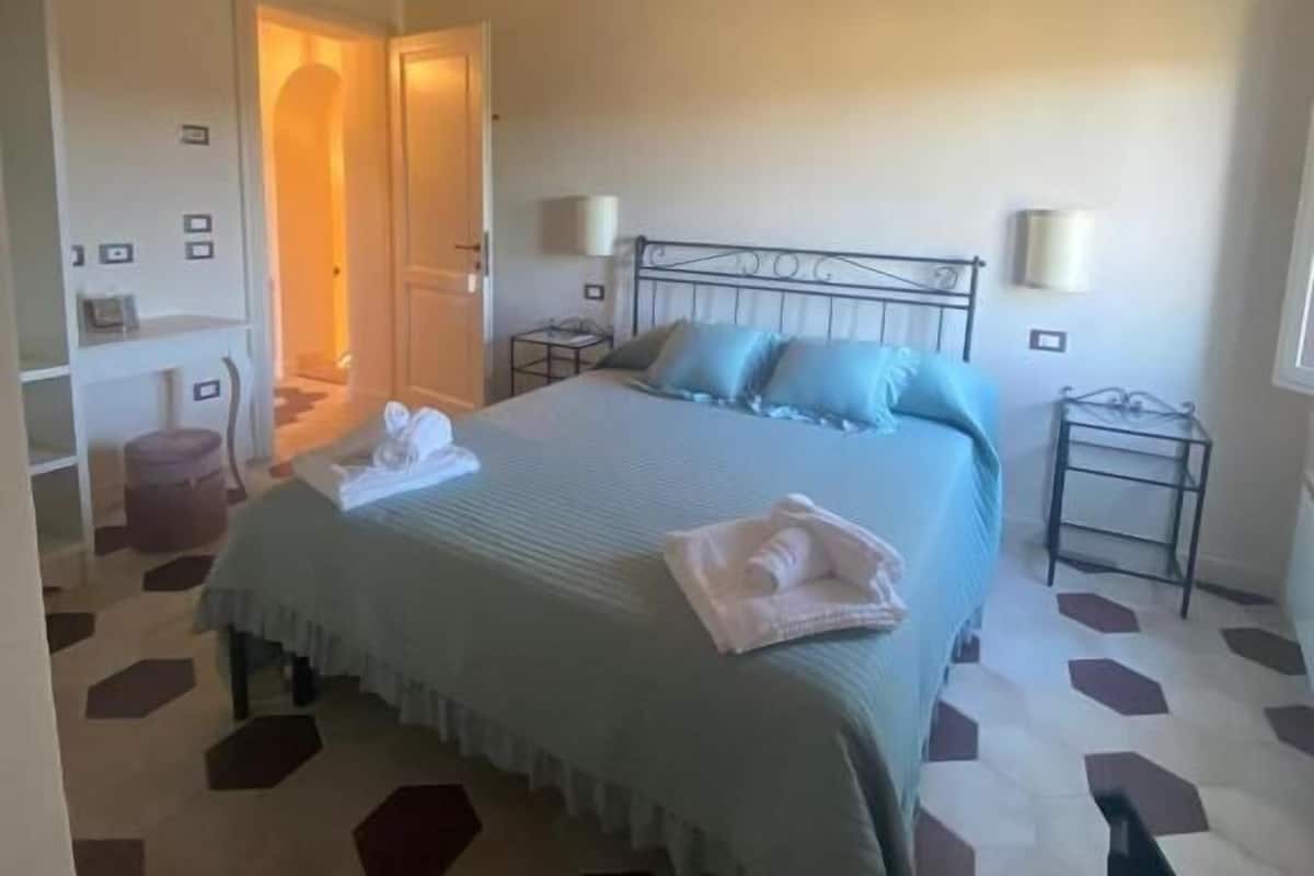 Quarto com cama, luminárias de cabeceira, teto de madeira e padrão geométrico no chão.