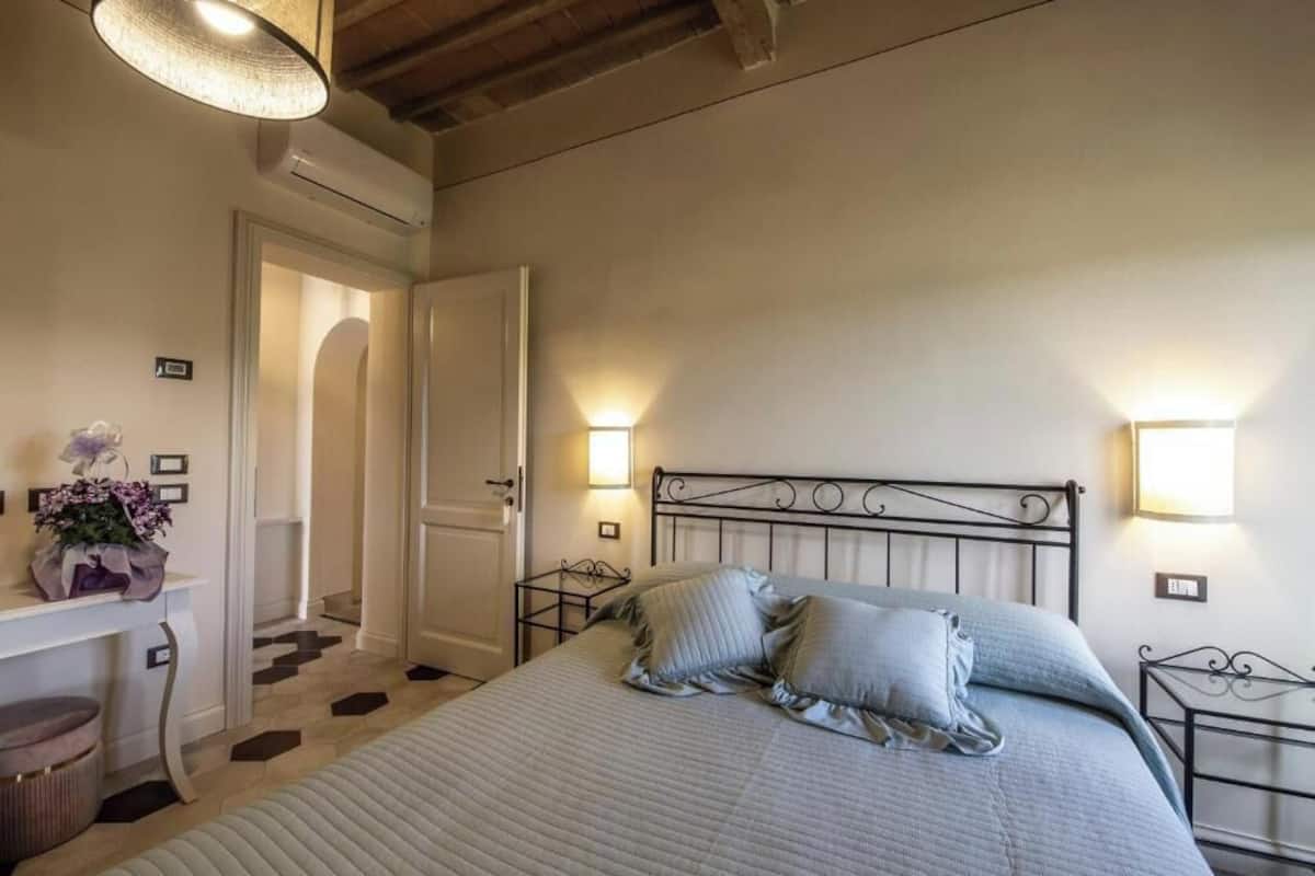 Quarto com cama, mesas de cabeceira, escrivaninha e abajur.
