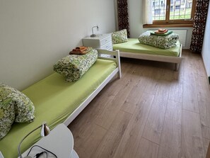 A room with two single beds, a desk, and a window with curtains. - Sut Via 19, Surcuolm, (Surcuolm), 38005B by Interhome (Surcuolm (Obersaxen))