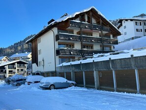 Ein mehrstöckiges Hotel mit Balkonen, ein Ski-Hang im Hintergrund und verschneite Umgebung.
