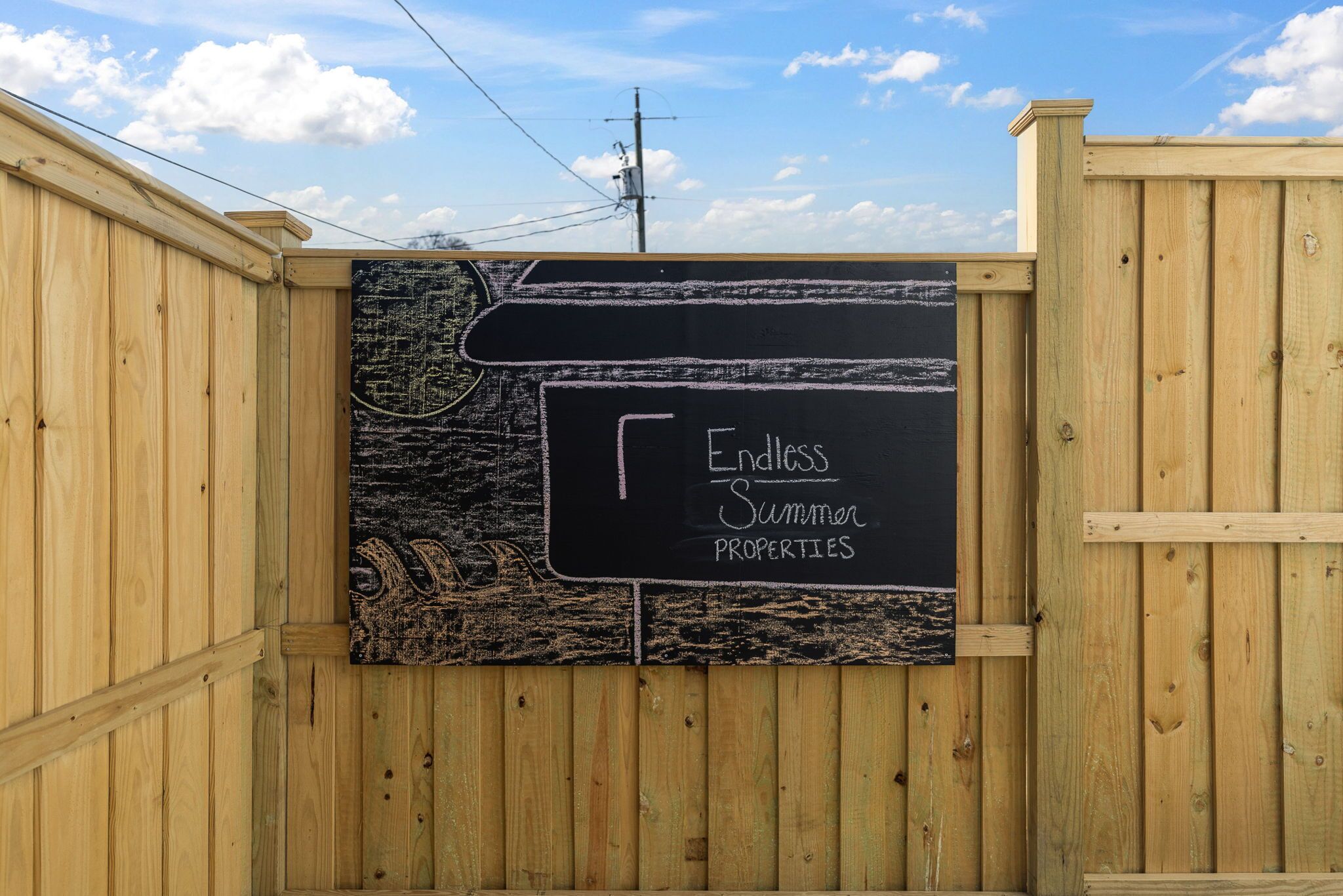 Cerca de madeira com uma placa de lousa anunciando 'Endless Summer Properties'.