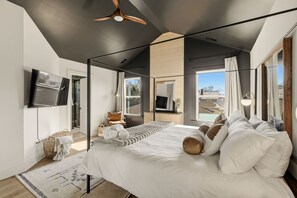 Een slaapkamer met een groot bed, een plafondventilator, een televisie en uitzicht op een zwembad.